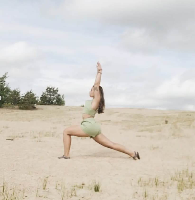 Woman doing a warrior yoga pose on a sand dune.
