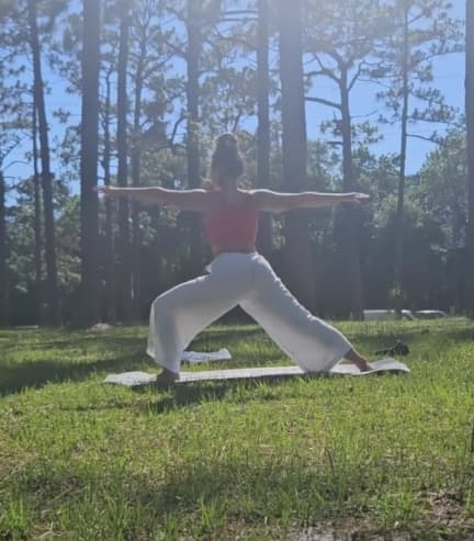 Person doing a yoga pose in a grassy, wooded area