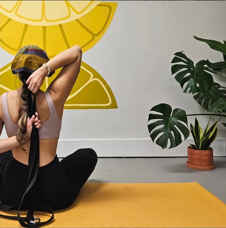 Woman practicing yoga poses against a wall with decorative lemon slice art and plants